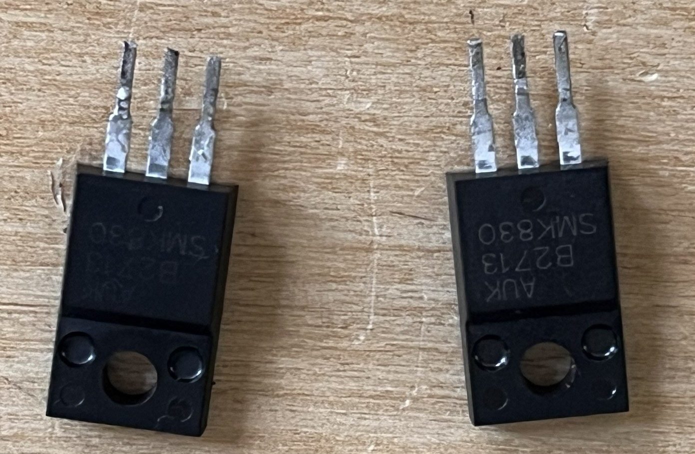 The two removed transistors lying side by side on a wooden surface, each marked AUK SMK830.