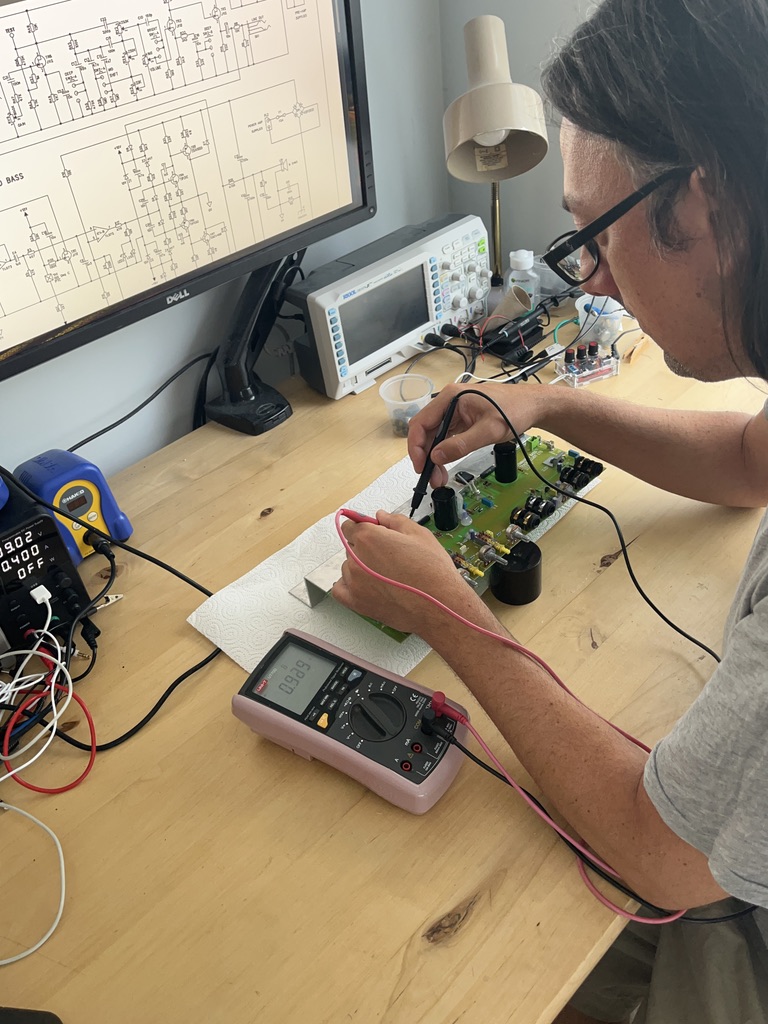 Jim at the workbench, probing a circuit board with a multimeter